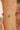 Gold bracelet with green and red beads on a wrist against a neutral background