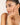 Woman touching her face wearing a delicate bracelet with a neutral background