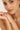 Close-up of a woman's face with a bracelet on her wrist against a neutral background