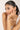 Woman with a ponytail touching her face wearing a delicate bracelet against a plain background