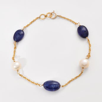 Gold bracelet with blue stones and pearls on a white background