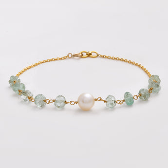 Gold bracelet with green beads and a pearl on a light gray background