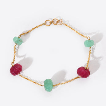 Bracelet with gold chain and green and red beads on a white background