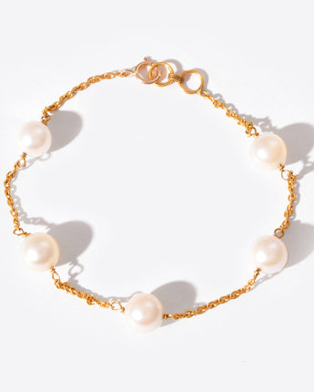 Gold chain bracelet with pearls on a white background