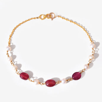 Gold bracelet with red gemstones and white pearls on a white background