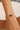 Gold bracelet with a blue gemstone and pearl on a wrist against a neutral background