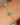 Gold bracelet with green beads on a wrist against a neutral background
