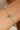 Gold bracelet with green beads on a wrist against a neutral background