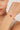 Close-up of a woman's wrist wearing a gold bracelet with red gemstones on a neutral background
