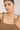 Woman wearing a brown tank top and pearl necklace against a plain background