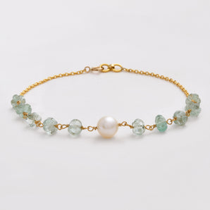 Gold bracelet with green beads and a pearl on a light gray background