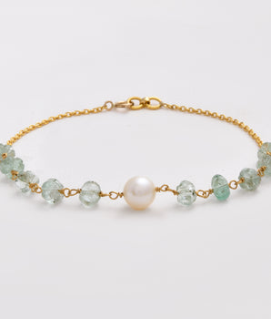 Gold bracelet with green beads and a pearl on a light gray background