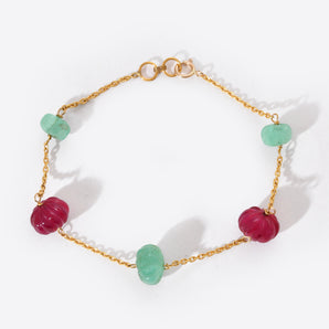 Bracelet with gold chain and green and red beads on a white background