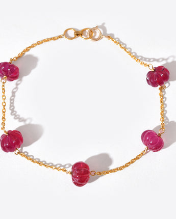 Gold bracelet with red beads on a white background