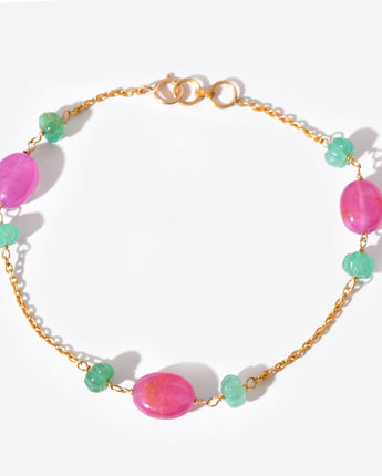 Bracelet with pink and green beads on a gold chain against a white background