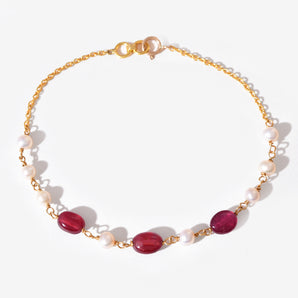 Gold bracelet with red gemstones and white pearls on a white background