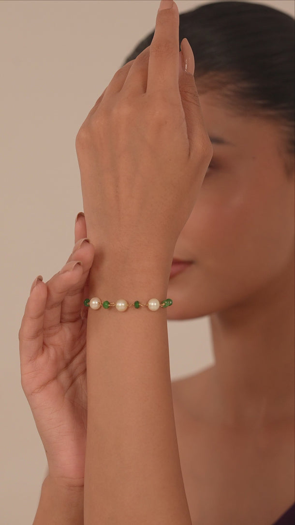 Woman wearing a bracelet with white pearl and green gemstones